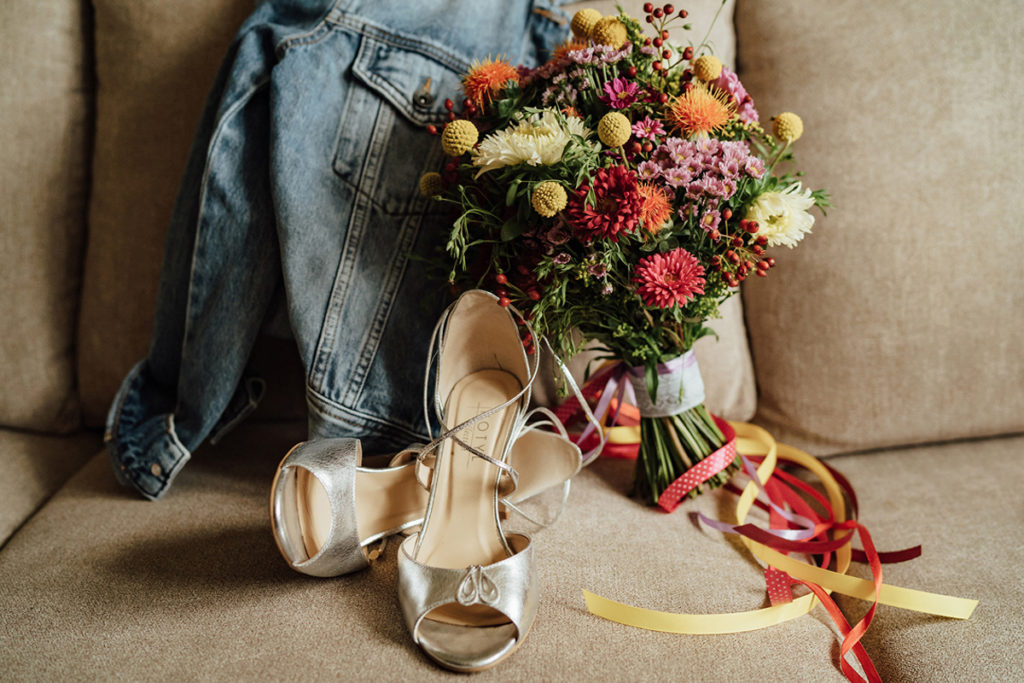 Detale ubioru Panny Młodej: srebrne buty do ślubu, kolczyki, jeansowa kurtka oraz bukiet z polnych kwiatów.